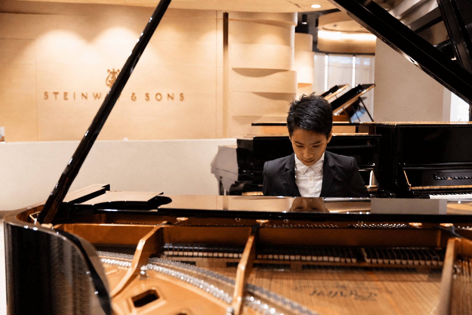 Matt.YC seated alone at a grand piano in a Steinway showroom